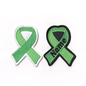 May include: Two green ribbon patches, one with a white background and the other with a black background. The black background patch has the word "Name" embroidered on it.