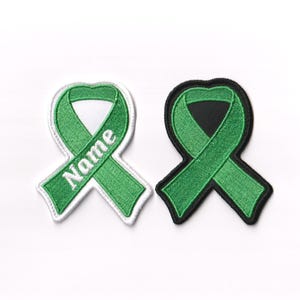 May include: Two green ribbon patches, one with a white background and the word "Name" embroidered on it, and the other with a black background.