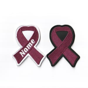 May include: Two burgundy ribbon patches, one with white outline and the word "Name" embroidered on it, and the other with a black outline.