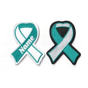 May include: Two embroidered awareness ribbon patches. One is teal and white with the word "Name" on the ribbon. The other is teal and white with a black border. Both are on a white background.