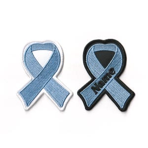 May include: Two light blue ribbon patches. One patch is white with a light blue ribbon. The other patch is black with a light blue ribbon and the word "Name" embroidered on it.
