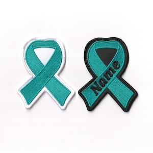 May include: Two teal ribbon patches, one with a white border and the other with a black border. The black bordered patch has the word "Name" embroidered on it.