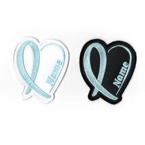 May include: Two heart-shaped patches. One is white with a light blue ribbon design and the word "Name". The other is black with a light blue ribbon design and the word "Name". Both patches have a stitched appearance.