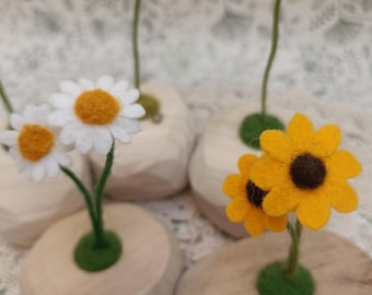 May include: A collection of handmade felt flowers, including daisies and sunflowers, in small wooden vases. The flowers have white or yellow petals with orange or brown centres and green stems. The vases are round with a flat base.