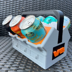 May include: A gray and orange six-pack cooler with a black handle. The cooler is filled with six cans of Kona Brewing Company "Liquid Aloha" beer. The cans are surrounded by ice.
