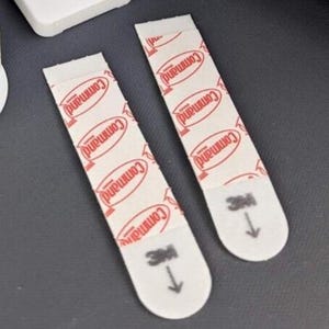 Puede incluir: Dos tiras adhesivas blancas de la marca Command con letras rojas. Las tiras están diseñadas para colgar objetos en las paredes.