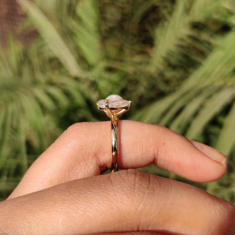 Peut inclure: Une bague en or avec une grosse pierre pr&eacute;cieuse blanche de forme ovale. Le corps de la bague est dor&eacute; et poli, et la pierre est sertie de petites pierres claires. La bague est pr&eacute;sent&eacute;e sur un fond vert flou.