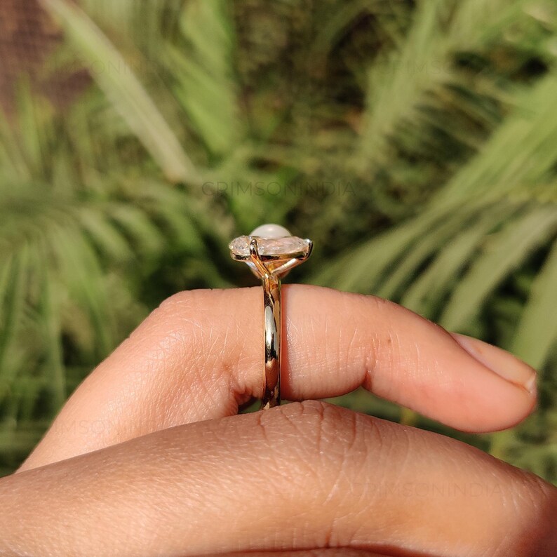 Peut inclure: Une bague en or avec une grosse pierre pr&eacute;cieuse blanche de forme ovale. La bague a un sertissage d&eacute;licat et d&eacute;taill&eacute; et un anneau en or poli. La pierre pr&eacute;cieuse est entour&eacute;e de petites pierres claires.