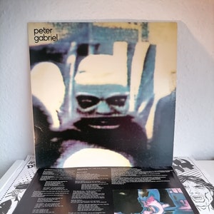 Könnte beinhalten: Ein schwarzes und weißes Vinyl-Albumcover mit einem verschwommenen Bild eines Gesichts. Das Album trägt den Titel "Peter Gabriel" und der Songtitel ist "Kiss of Life".