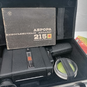 May include: A black vintage Aurora 2150 film camera in a black carrying case with a green filter and a Russian language instruction manual. The camera has a silver star logo and the text "Aurora 2150 made in USSR" on the top.