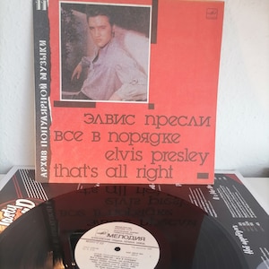 May include: A red and black vinyl record album cover featuring a black and white photo of Elvis Presley. The album title is "Elvis Presley - That's All Right" in Russian and English. The album is from the "Melodiya" record label.