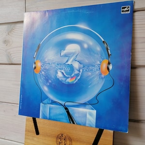 May include: A blue vinyl record cover with a large, transparent sphere containing a number "3" and a pair of headphones with orange earcups. The text "Музыкальный Третий" is visible on the sphere.