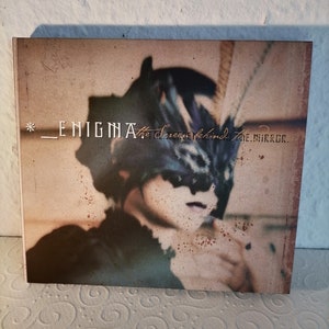 May include: A CD cover with a vintage aesthetic featuring a person wearing a mask and the text "* _ENIGMA_ The Screen Behind The Mirror."