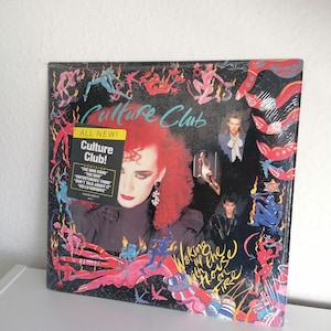 Puede incluir: Un álbum de vinilo de Culture Club, titulado "Waking Up With The House On Fire". La portada presenta un retrato de una persona con cabello rojo y maquillaje, rodeada de ilustraciones coloridas y texto. El álbum está sellado en plástico.