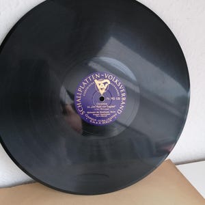 May include: A black vinyl record with a purple label. The label has the text " Schallplatten - Volksverband" and "Nr. MD 126" in gold lettering. The label also has a small image of a harp.