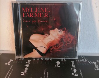 Puede incluir: Una caja de CD con un fondo rojo y una mujer con cabello rojo en la portada. El título del CD es "MYLENE FARMER Avant que l'ombre..."