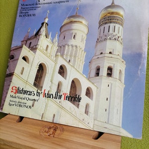 May include: A vintage vinyl record with a picture of a white building with gold domes. The record is titled "Sticheras by Ivan the Terrible" and features a male vocal quartet. The record is on a wooden stand.