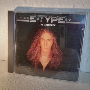 May include: A CD case with a black background and the text "E-TYPE" and "the explorer" in white. A man with long curly red hair is pictured on the front of the case.