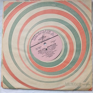 Puede incluir: Una funda de disco de vinilo vintage con un patrón de círculos concéntricos rojo y verde. La etiqueta presenta el texto "Мелодия" en una fuente estilizada, junto con el título "ПЕСНИ ПОЛАЯ БЮЛЬ-БЮЛЬ-Оглы" y una lista de títulos de canciones.
