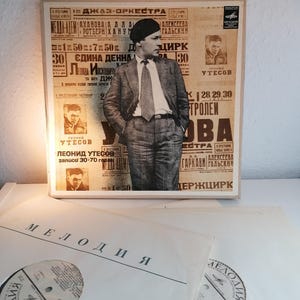 May include: A vintage record album cover featuring a black and white photo of a man in a suit and tie. The album cover is titled "Melodiya" and features the text "Leonid Utesov" and "Jazz Orchestra".