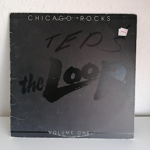 Può includere: Un disco in vinile nero con il testo "Chicago Rocks" e "TEP'S the Loop VOLUME ONE" in bianco. La copertina del disco presenta un'illustrazione in bianco e nero di un loop.
