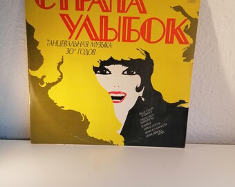 Puede incluir: Una portada de disco de vinilo amarilla con el título "Страна Улыбок" en letras rojas. La portada presenta una ilustración en blanco y negro de una mujer con una sonrisa roja. El texto "Танцевальная музыка 30-х годов" también está en la portada.