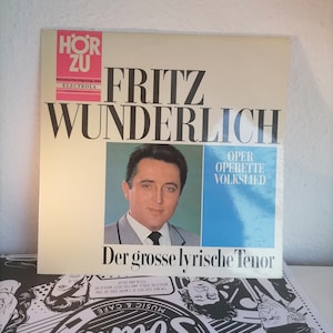 May include: A vintage vinyl record cover featuring a portrait of Fritz Wunderlich, a German tenor, with the text "Fritz Wunderlich Der grosse lyrische Tenor" and "Oper Operette Volkslied" in black and white. The background is a light blue.