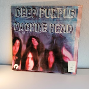 May include: Album cover for Deep Purple's "Machine Head." The album art features the band's name and album title in a raised, white font against a blue and purple background. The cover also shows the band members' faces.