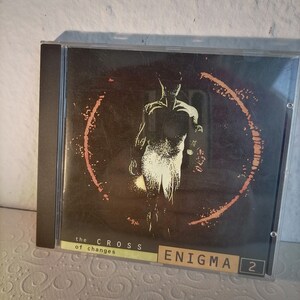 Könnte beinhalten: Ein CD-Gehäuse mit einem schwarzen und orangefarbenen Design. Die Vorderseite des Gehäuses zeigt eine Silhouette einer Person, die in einem Kreis steht. Der Text "the CROSS of changes" und "ENIGMA 2" ist auf dem Gehäuse aufgedruckt.