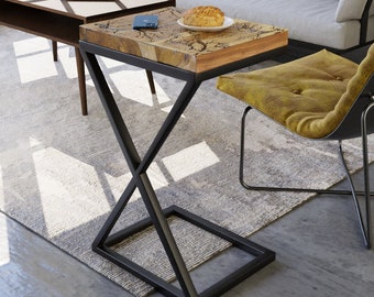 May include: A small wooden side table with a black metal X-shaped base. The table has a natural wood top with a rustic finish. The table is next to a gray sofa and a yellow chair.