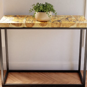 Peut inclure: Une console en bois avec une finition en bois naturel et un cadre en métal noir. La table a un plateau rectangulaire et est soutenue par quatre pieds. Une petite plante en pot est posée sur la table.