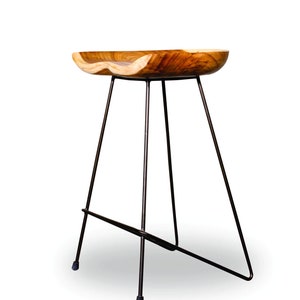 Peut inclure: Tabouret de bar en bois avec une assise incurv&eacute;e naturelle et des pieds en m&eacute;tal fonc&eacute;. L'assise est en bois brun clair avec un motif de grain unique. Les pieds sont fins et inclin&eacute;s, offrant un design moderne et minimaliste.
