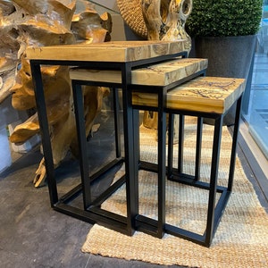 Op de afbeelding: Drie geneste houten tafels met zwarte metalen frames. De tafels zijn gemaakt van natuurlijk hout met een uniek graanpatroon. De tafels zijn op elkaar gestapeld, met de grootste tafel onderaan en de kleinste tafel bovenaan.