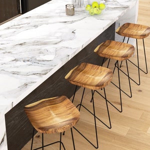 Peut inclure: &Icirc;lot de cuisine moderne avec un plan de travail en marbre blanc et quatre tabourets de bar en bois. Les tabourets ont des assises en bois naturel et des pieds en m&eacute;tal noir. Le sol est en bois clair. Un four en acier inoxydable est visible.