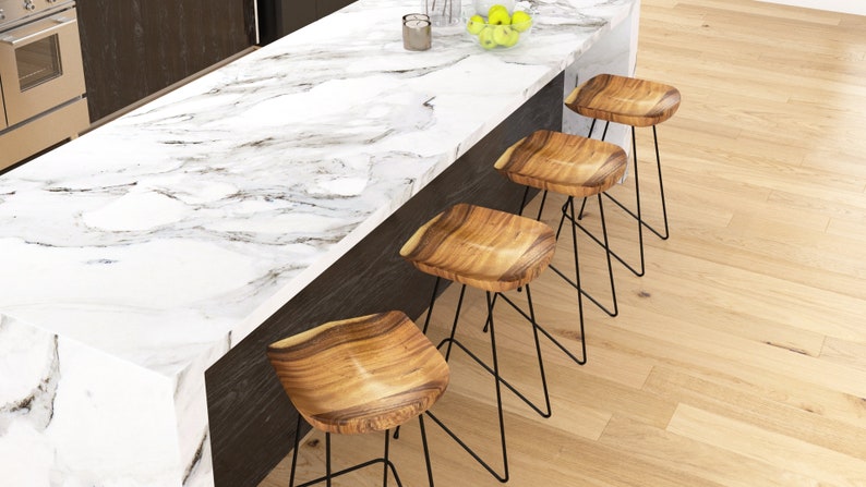 Peut inclure: &Icirc;lot de cuisine moderne avec un plan de travail en marbre blanc et quatre tabourets de bar en bois. Les tabourets ont des assises en bois naturel et des pieds en m&eacute;tal noir. Le sol est en bois clair. Un four en acier inoxydable est visible.