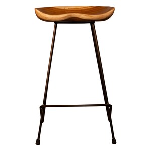 Peut inclure: Tabouret de bar en bois avec une assise profil&eacute;e et des pieds en m&eacute;tal fonc&eacute;. L'assise est en bois clair avec un motif de grain naturel. Les pieds sont fins et inclin&eacute;s, avec un repose-pieds pr&egrave;s de la base. Le tabouret a un design moderne et minimaliste.