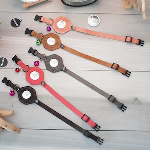 May include: Four different leather dog collars with a small mirror and a bell attached. The collars are in pink, brown, gray, and red.