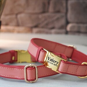 May include: Two pink leather dog collars with gold metal buckles. The larger collar has a gold tag with the name "Valery" and phone number "321-654-4895" engraved on it.