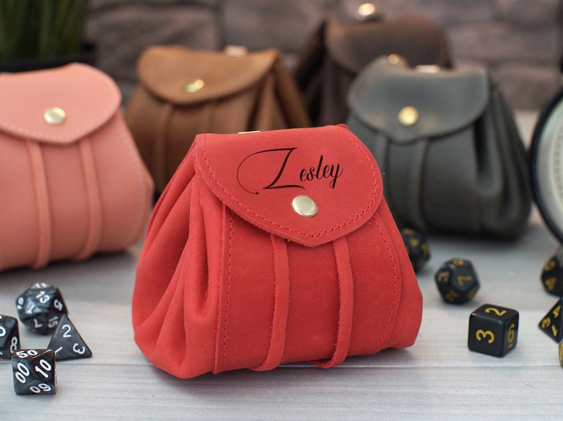 Pode incluir: Saco de dados de couro vermelho com fecho de aba e bot&atilde;o dourado. O saco &eacute; personalizado com o nome "Lesley" em escrita cursiva. O saco &eacute; rodeado por dados pretos.