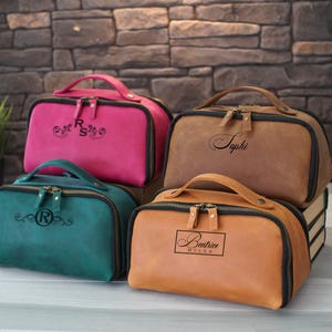 Può includere: Quattro trousse da toilette in pelle personalizzate in diversi colori. Le trousse hanno cerniere nere e sono decorate con nomi e iniziali ricamate. Le trousse sono disposte su una superficie in legno.