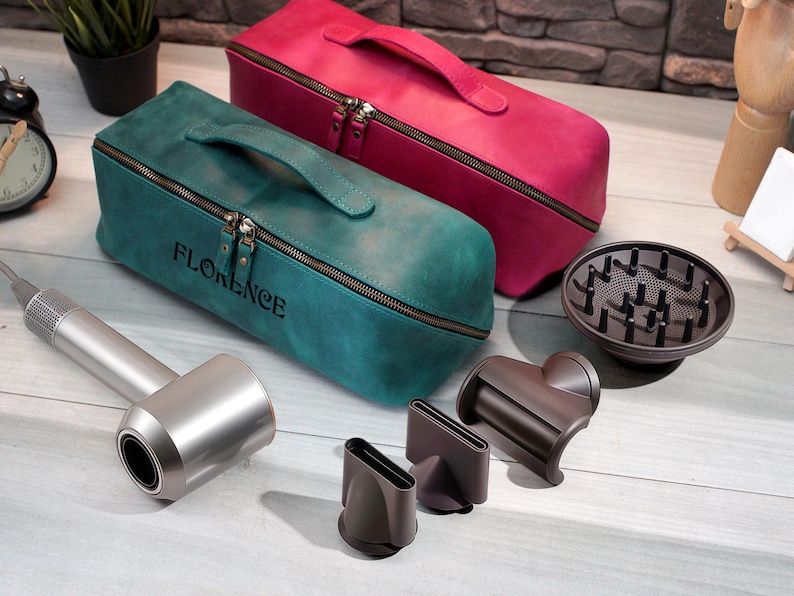 May include: A teal and a magenta leather travel case with a handle and zipper, with the name "FLORENCE" embossed on the teal case. A silver hair dryer and attachments are also visible, including a diffuser and nozzles.