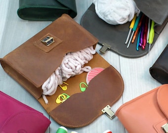 May include: A collection of brown leather bags with different coloured interiors. The bags are open and show various items inside, including yarn, crochet hooks, and stitch markers.