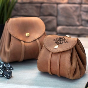 May include: Two brown leather pouches with drawstrings. The larger pouch is plain, while the smaller pouch has the name "DEBRA" engraved on the front flap.