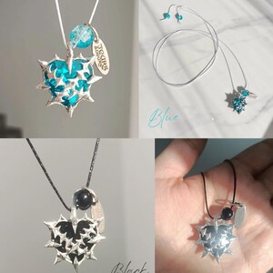 May include: Two necklaces with a silver heart pendant with spikes and a small charm. The heart pendant is blue on one necklace and black on the other. The necklaces are on white and black cords.