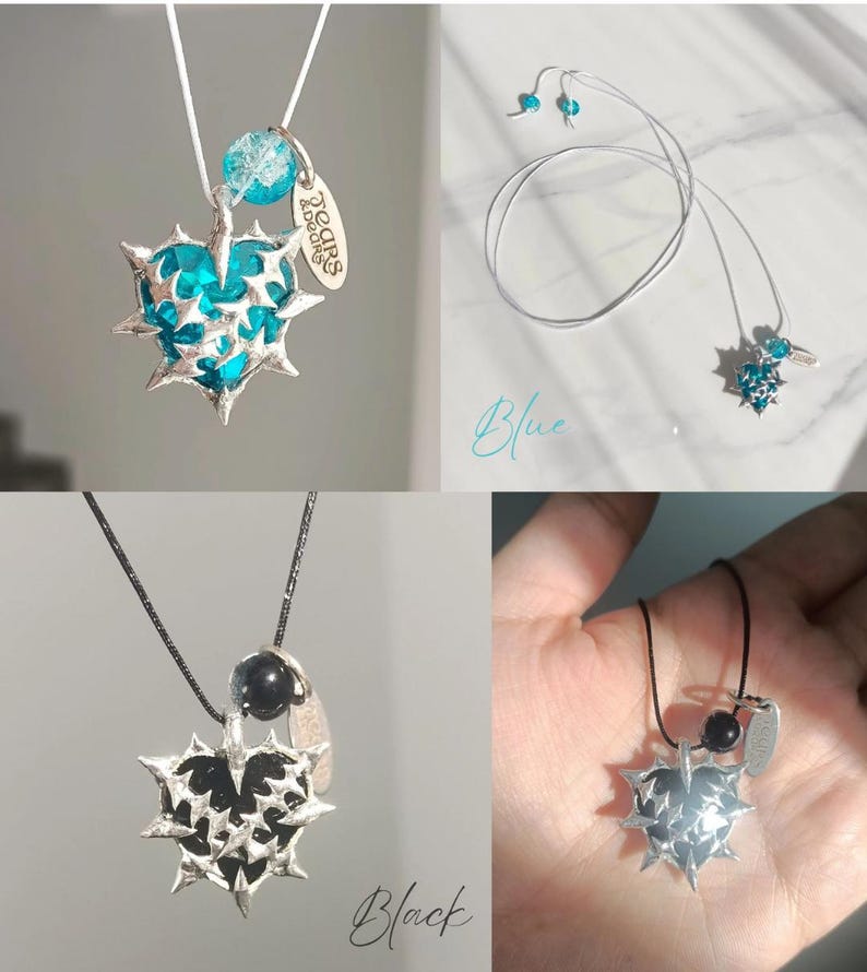 May include: Two necklaces with a silver heart pendant with spikes and a small charm. The heart pendant is blue on one necklace and black on the other. The necklaces are on white and black cords.