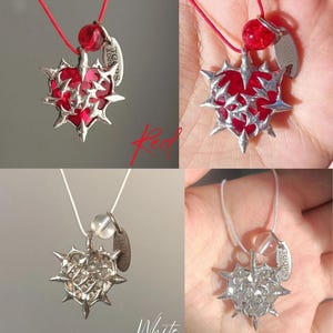 May include: A silver necklace with a red heart pendant. The heart is covered in spikes and has a silver tag that says "Saddles & Love".