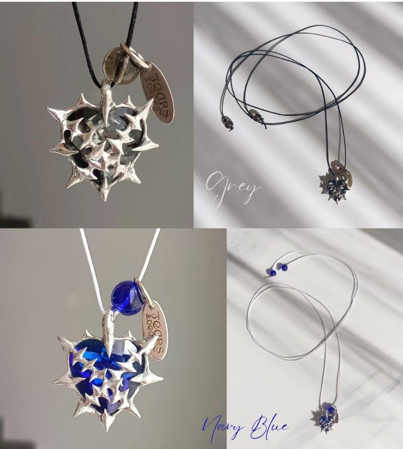 May include: A silver heart-shaped pendant necklace with a blue glass gem in the center. The pendant is surrounded by silver spikes and has a small silver tag that says "Tears & Beads". The necklace is available in grey and navy blue.