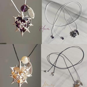 May include: Two silver heart-shaped pendants with thorns, one with a purple stone and the other with a yellow stone. Both pendants are on black and white cords with small beads.
