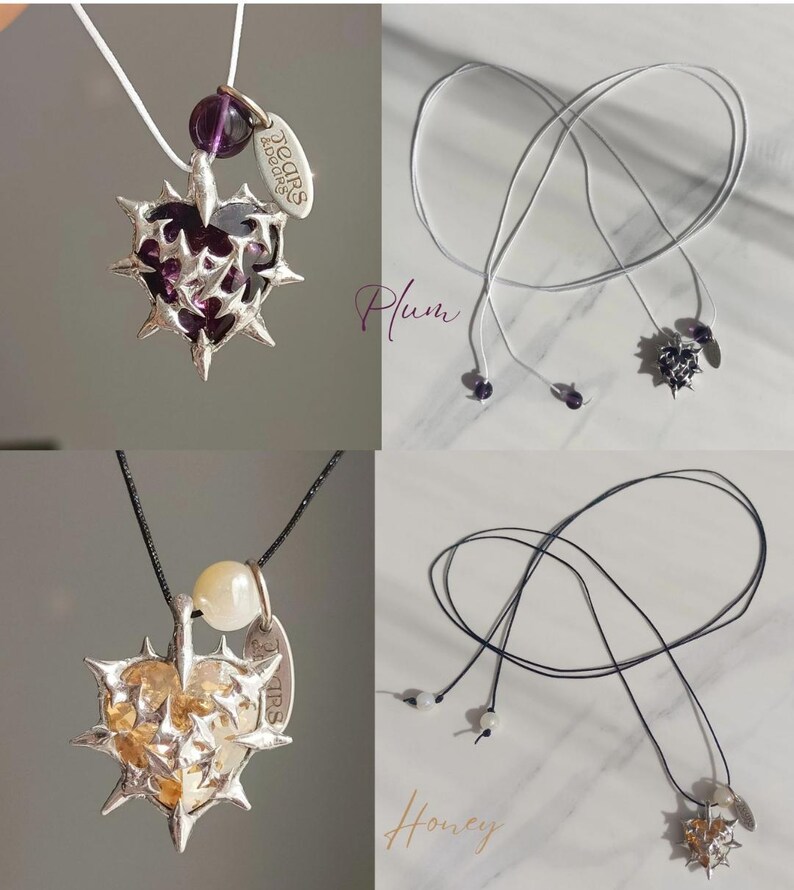 May include: Two silver heart-shaped pendants with thorns, one with a purple stone and the other with a yellow stone. Both pendants are on black and white cords with small beads.