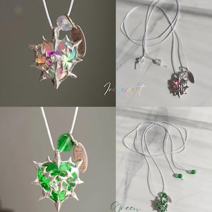 May include: Two necklaces with a heart-shaped pendant with a thorny design. The pendant on the left is iridescent and the pendant on the right is green. Both pendants have a small tag that says "Yours Forever".